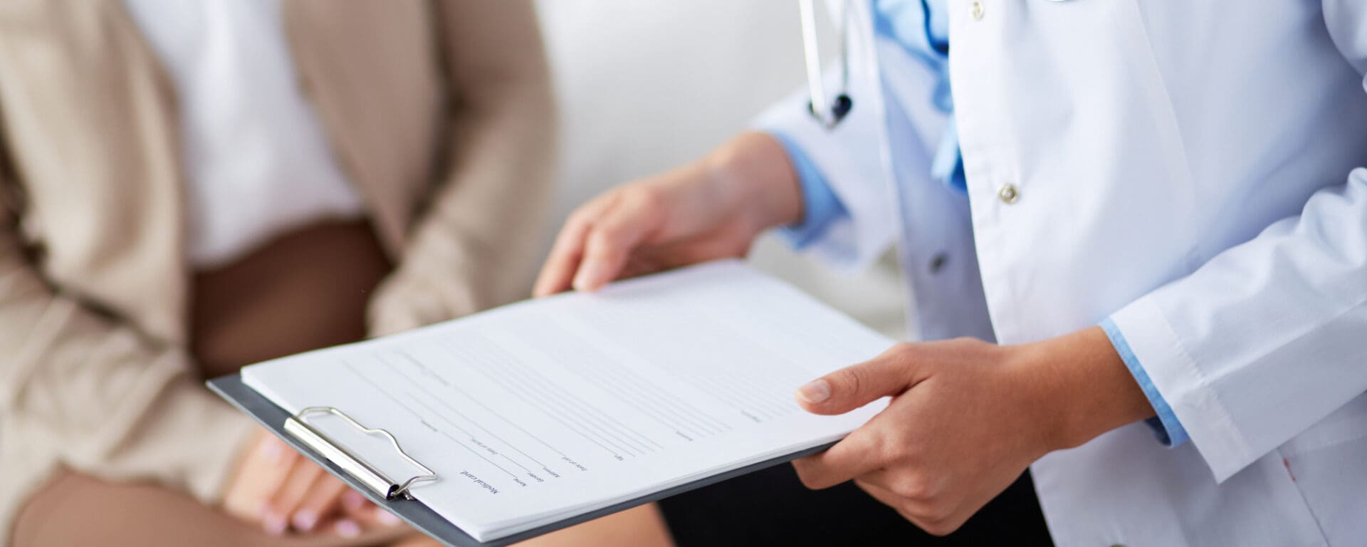 Doctor holding a clipboard with a patient in the background.